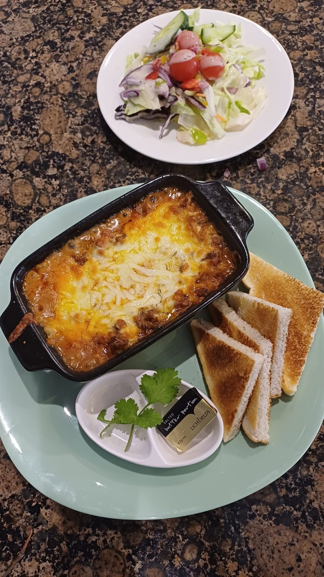 A cheesy baked dish with toast and salad
